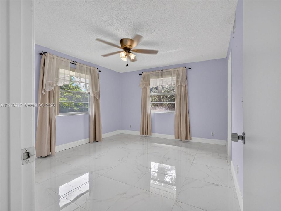 Large-format polished tile flooring, ceiling fan with integrated lighting, and multiple windows providing natural light
