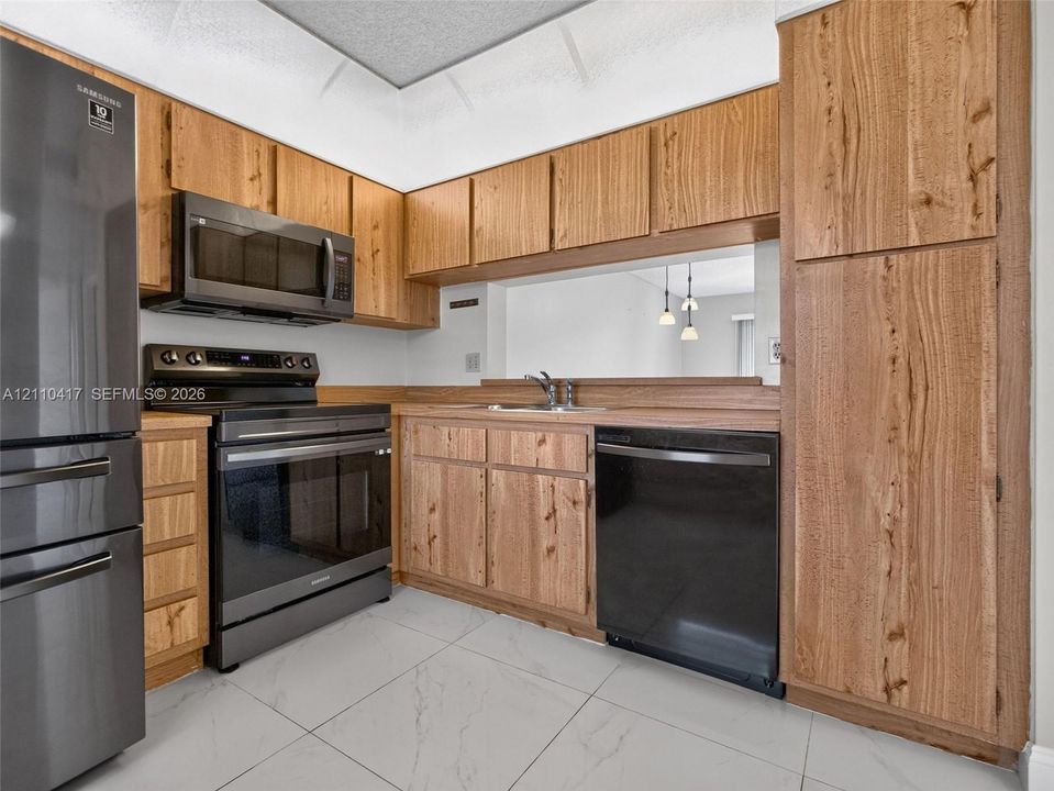 Kitchen featuring wood cabinetry, stainless steel appliances, a pass-through opening, and large-format tile flooring