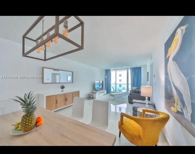 Open-concept main living area featuring glossy tile flooring, a geometric metal-frame chandelier, and floor-to-ceiling glass sliding doors