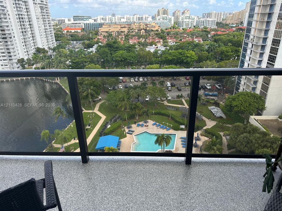 Balcony featuring a matte black metal railing and textured flooring, overlooking a community swimming pool, landscaped grounds, and a water feature