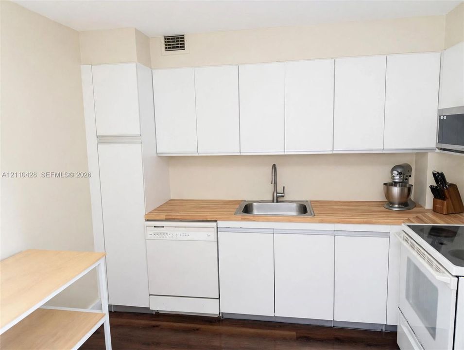 Kitchen featuring white slab-front cabinetry, wood-finish countertops, stainless steel sink with high-arc faucet, and wood-finish flooring