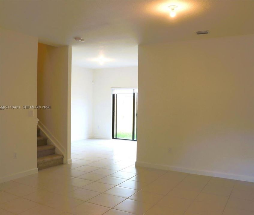 Interior space featuring neutral wall paint, tile flooring, flush-mount ceiling lighting, carpeted staircase, and sliding glass doors