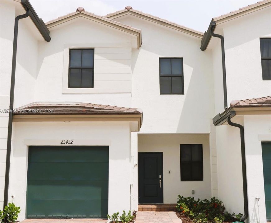 Exterior featuring a stucco facade, dark-toned garage door, gabled roofline, dark-framed multi-pane windows, and a paved entryway path