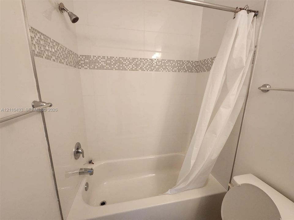 Bathroom featuring a tub and shower combination, white wall tiling, a decorative mosaic tile accent border, and chrome plumbing fixtures
