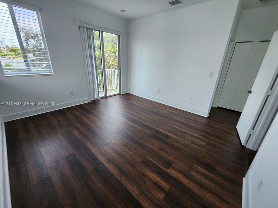 Room featuring wood-finish flooring, sliding glass doors to a balcony, and dual-panel closet doors