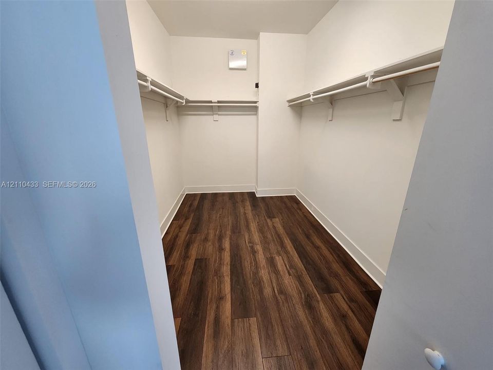 Walk-in closet featuring wood-finish flooring and dual-level built-in shelving with integrated rods