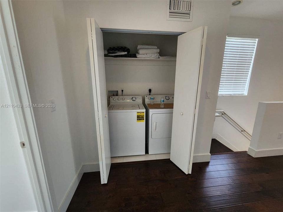 Closet laundry area featuring bifold doors, integrated shelving, and dark-toned wood-finish flooring