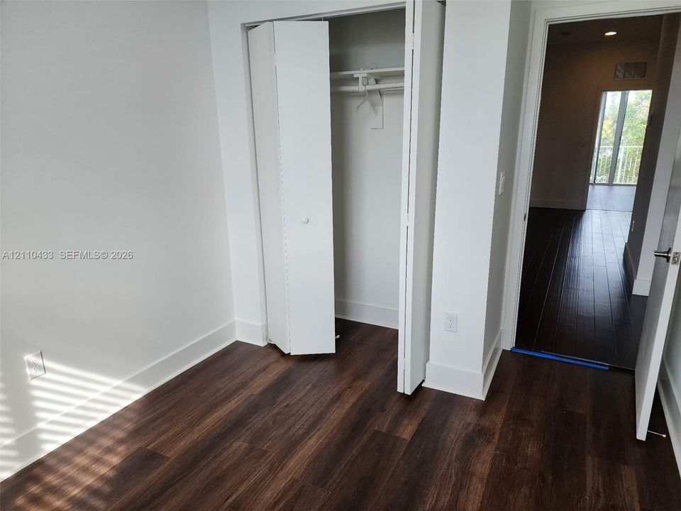 Room featuring dark wood-finish flooring, white walls, and a closet with bifold doors and built-in shelving