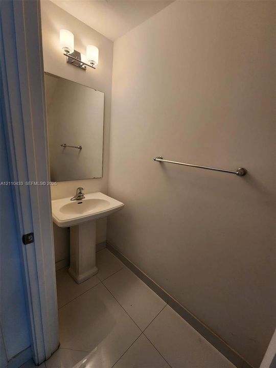 Powder room featuring a white pedestal sink, polished chrome faucet, rectangular wall-mounted mirror, dual-light vanity fixture, and tiled flooring