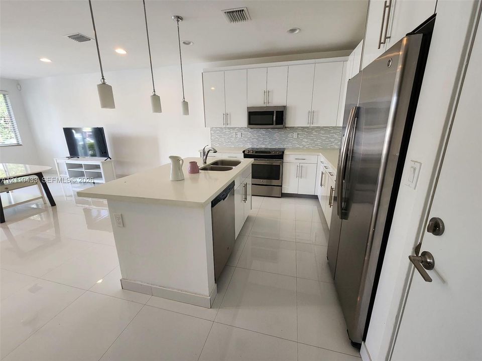 Kitchen featuring white cabinetry, quartz countertops, a center island with an integrated sink, stainless steel appliances, and large-format tile flooring
