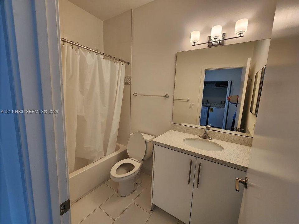 Bathroom featuring a vanity with a light-toned countertop, integrated basin, three-light wall-mounted fixture, frameless wall mirror, and a tub-shower combination