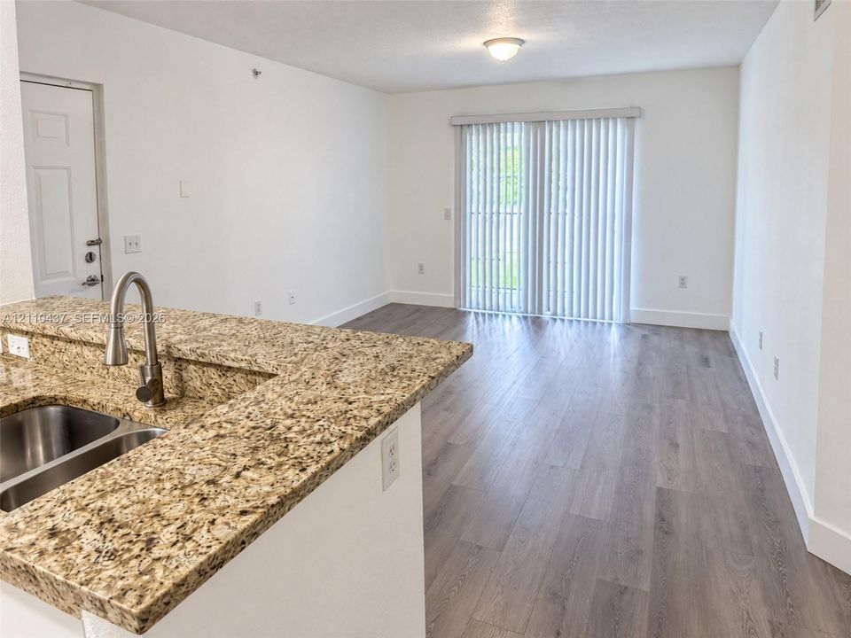 Stone-surfaced breakfast bar with a stainless steel undermount sink, gooseneck faucet, wood-finish flooring, and sliding glass doors with vertical blinds