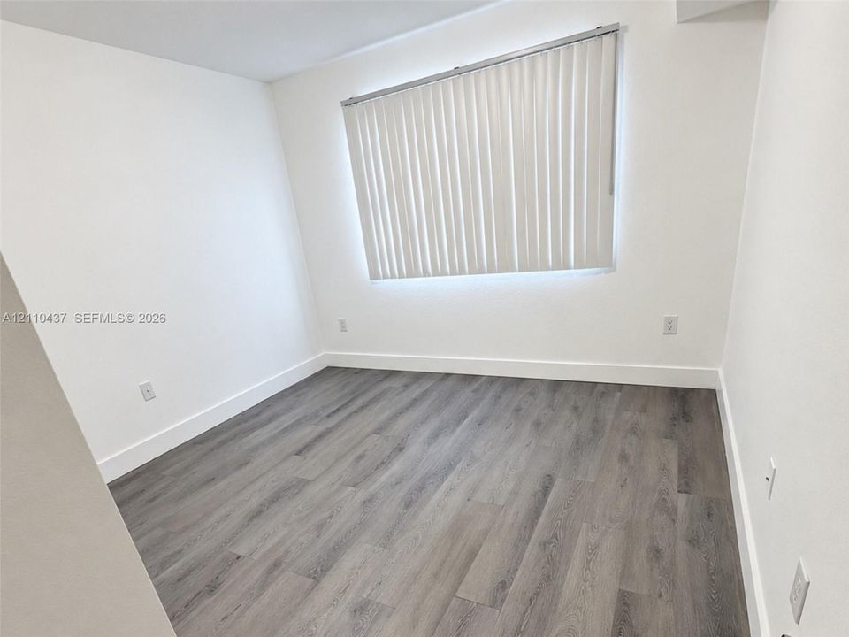 Interior space featuring neutral white walls and wood-finish flooring, complemented by a window outfitted with vertical blinds