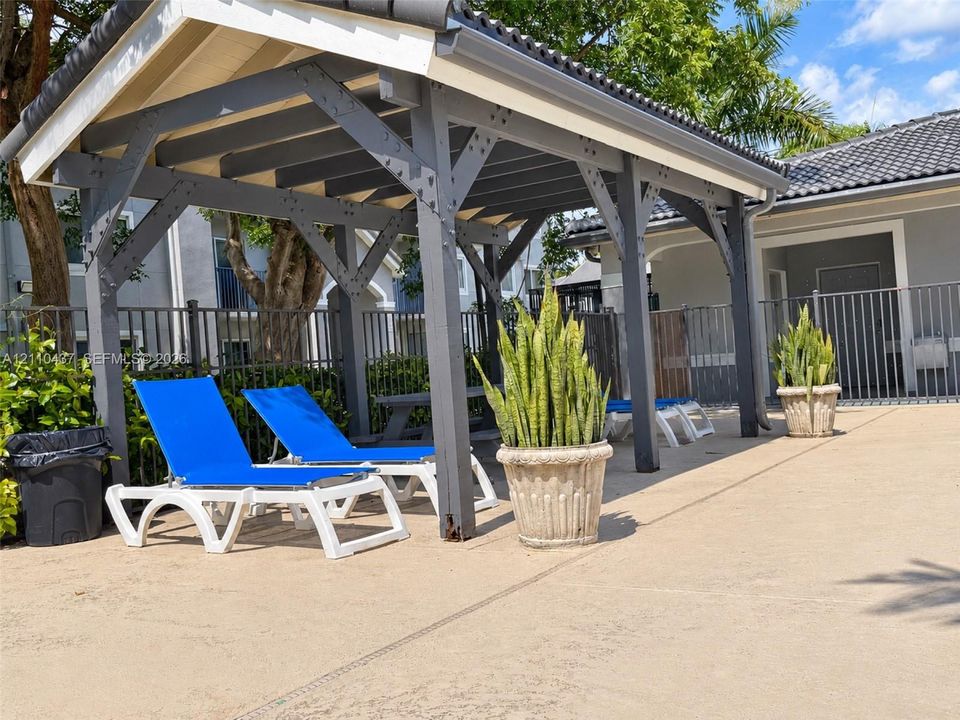 Covered pergola featuring dark-toned timber framing and a shingled roof, set atop a concrete deck with metal perimeter fencing