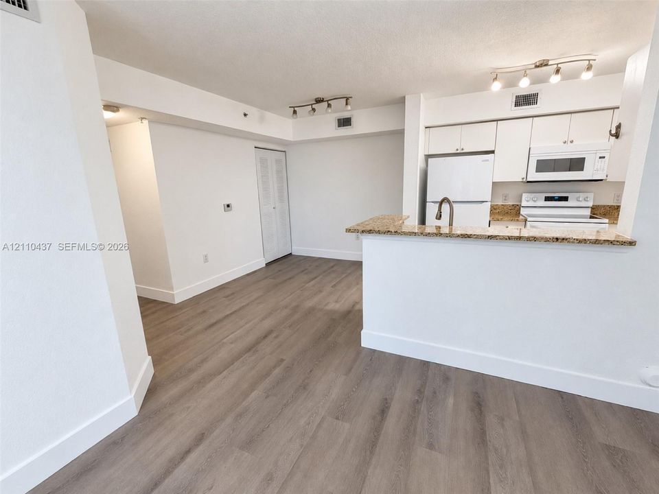 Kitchen featuring a stone-finish breakfast bar, white cabinetry, integrated microwave, wood-finish flooring, and multi-bulb track lighting