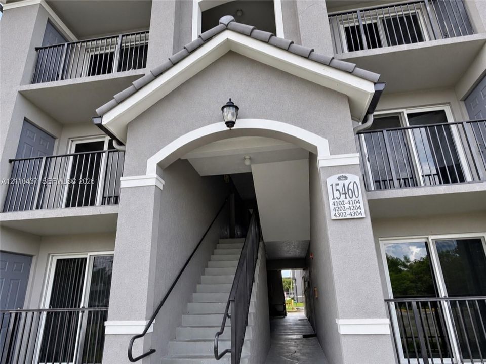 Stucco exterior featuring a pitched tile roof gable, arched entryway, private metal balconies, and concrete stairs with metal railings