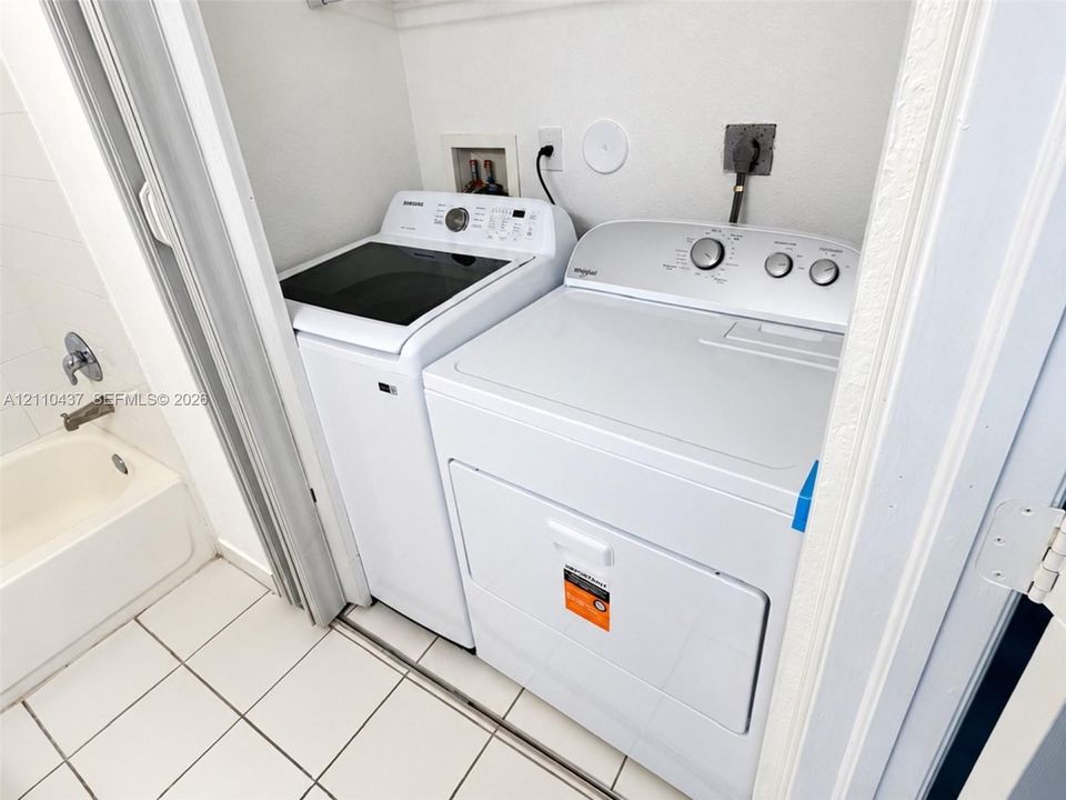 Utility closet featuring laundry hookups, white tile flooring, and a porcelain-finish bathtub with chrome faucet hardware
