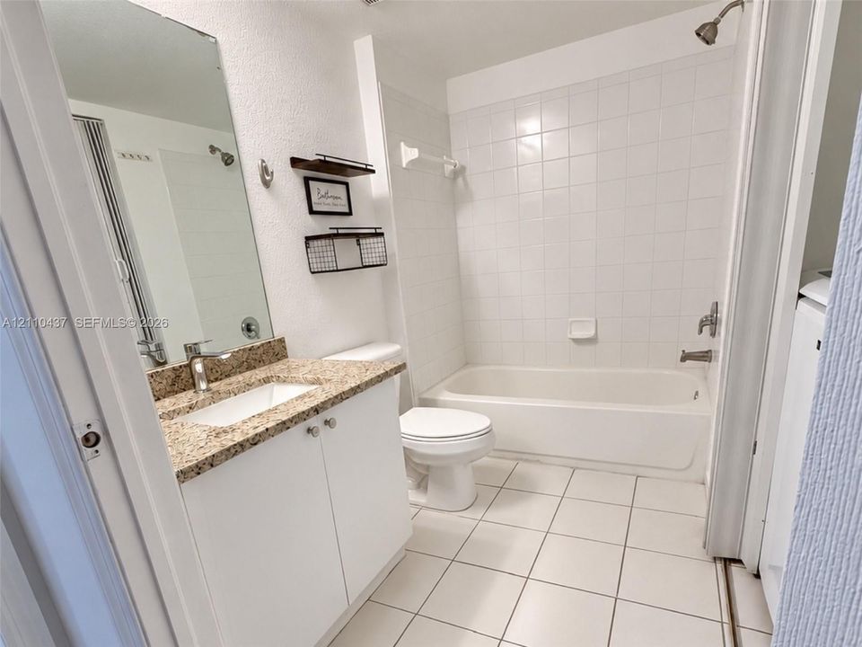 Bathroom featuring a white vanity cabinet with a stone-composite countertop, undermount sink, ceramic tile flooring, and a shower-tub combination with white wall tile