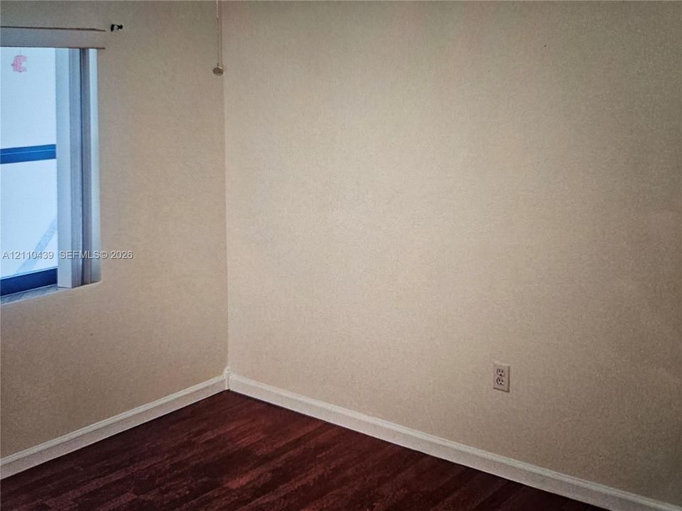 Room featuring wood-finish flooring, neutral-toned walls, and a single-pane window with a roller shade