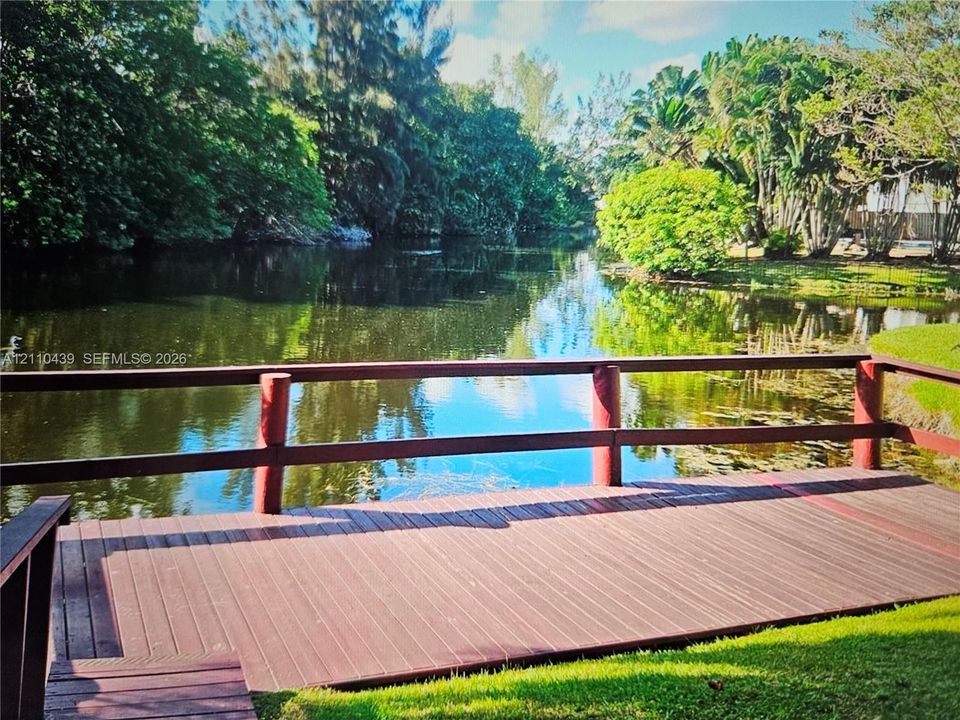 Waterfront wooden deck featuring perimeter railing and mature perimeter landscaping