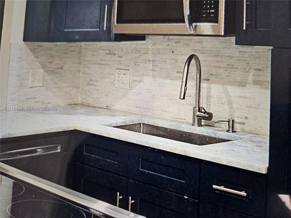 Kitchen featuring dark-toned cabinetry, light-toned stone-finish countertops, linear tile backsplash, stainless steel under-mount sink, and gooseneck pull-down faucet