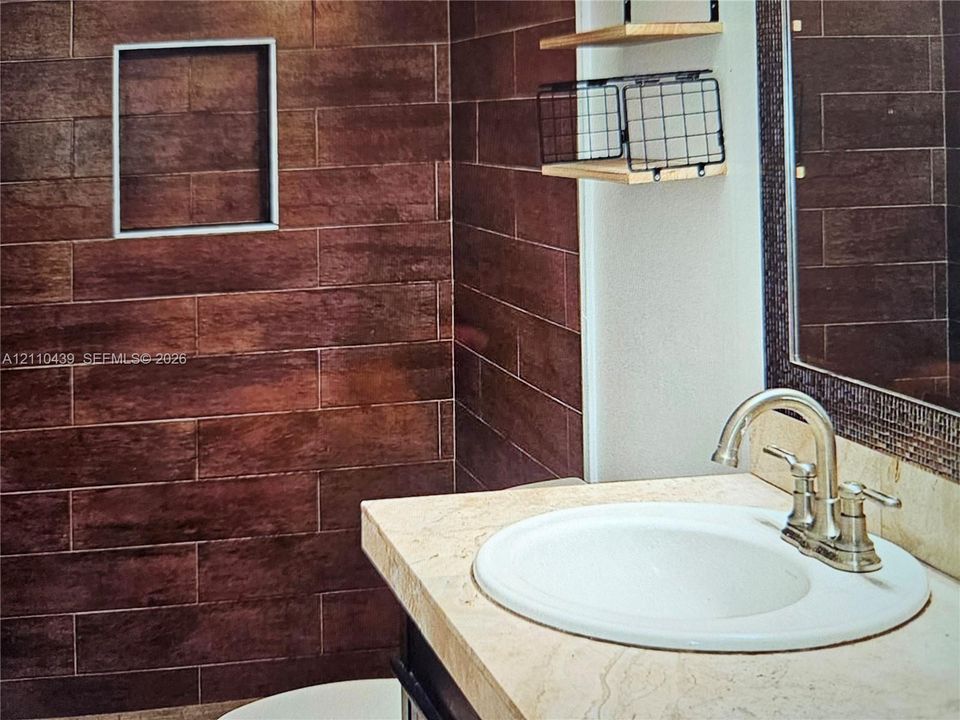 Rectangular vanity with a stone countertop, integrated ceramic sink, metallic dual-handle faucet, and horizontal plank-style wall tiling featuring a built-in recessed wall niche