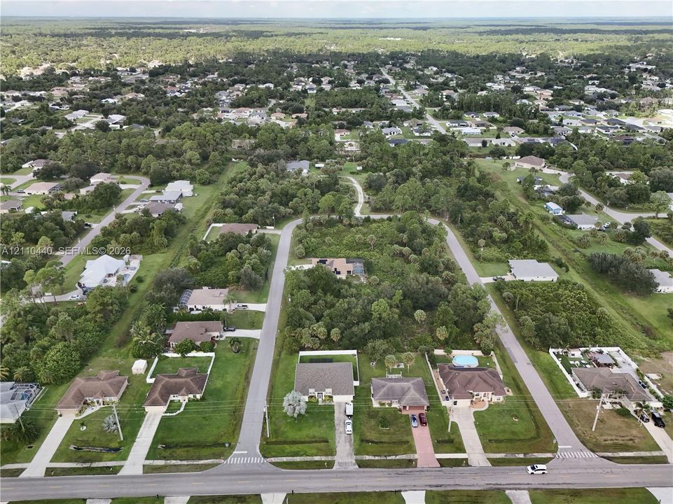 Aerial perspective of a suburban neighborhood featuring paved roads, established residential lots, mature vegetation, and expansive natural wooded areas