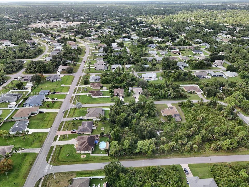 Aerial perspective of a suburban neighborhood featuring paved streets, mature trees, manicured lawns, and residential properties with varied roof pitches