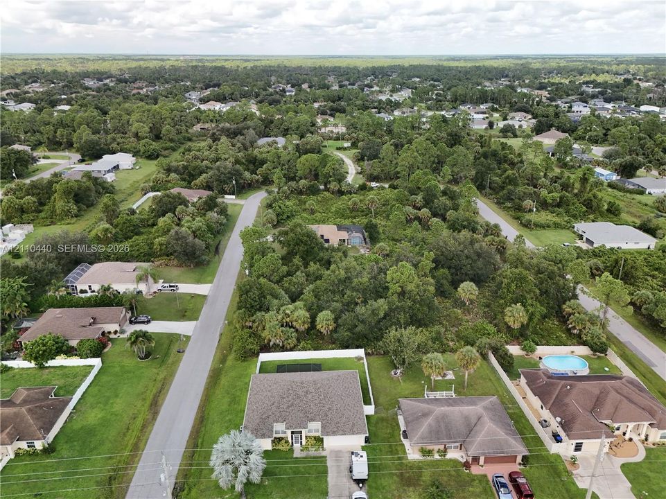 Aerial perspective of a residential lot featuring a multi-gabled roofline, private fenced perimeter, paved driveway, and mature landscaping