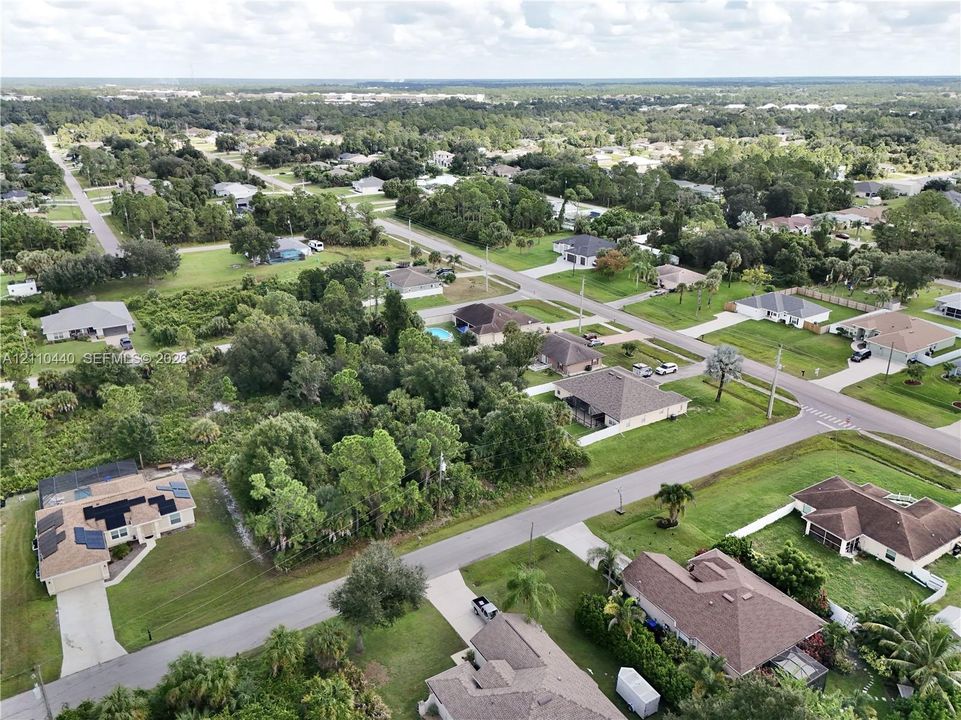 Aerial perspective featuring a residential lot with mature trees and proximity to paved road infrastructure