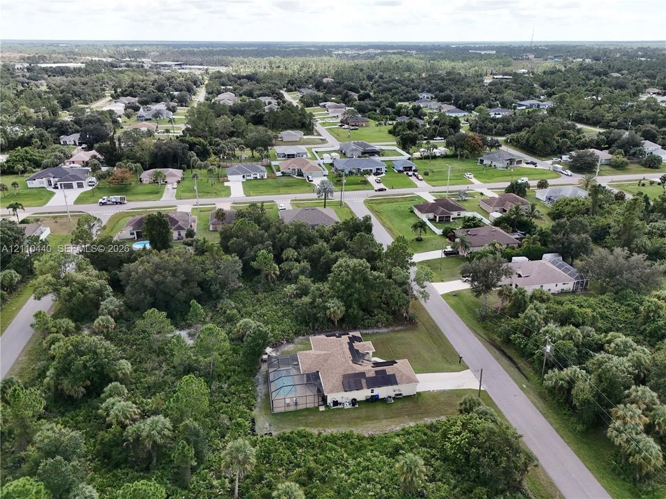 Aerial perspective of a single-family residence featuring a screened-in lanai with a swimming pool, a multi-gabled asphalt shingle roof, solar panels, and mature surrounding landscape