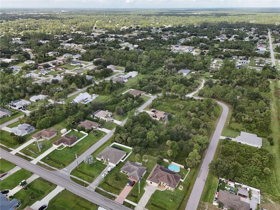 Aerial perspective of a residential neighborhood featuring paved streets, established tree canopy, grass-covered lots, and single-story detached structures