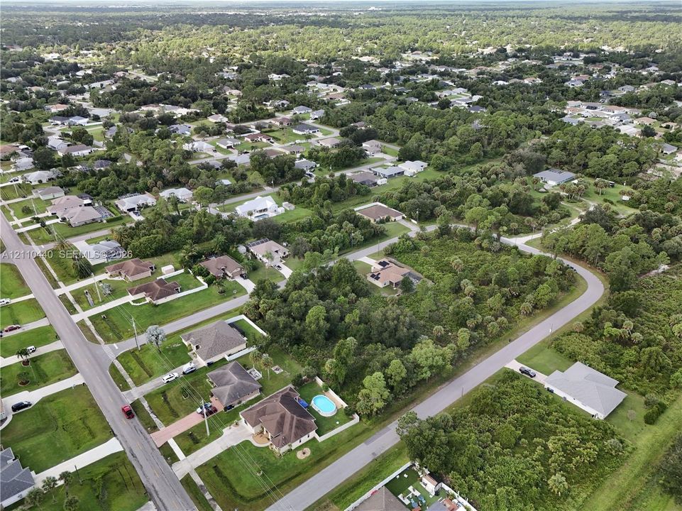 Aerial perspective featuring a low-density residential neighborhood with paved streets, abundant mature tree cover, and dispersed single-family homes