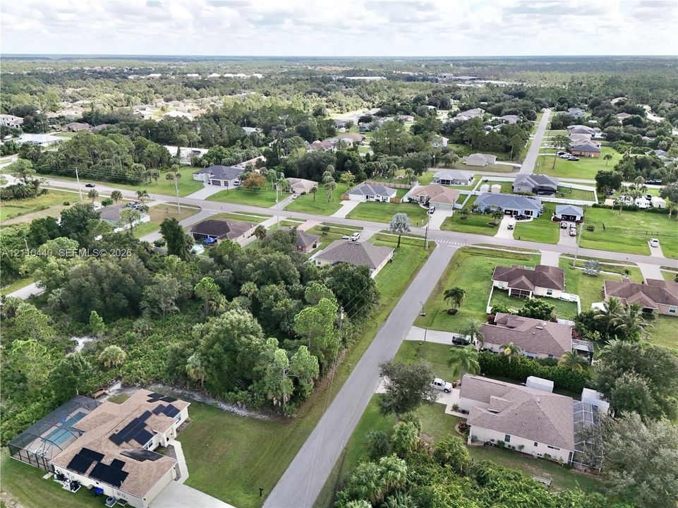 Aerial perspective of a residential property featuring an attached screened-in swimming pool enclosure and installed roof-mounted solar panels, situated on a lot with mature perimeter vegetation