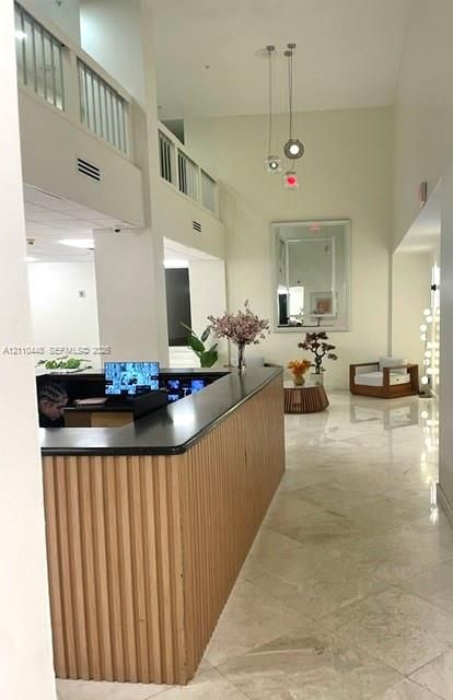High-ceilinged foyer featuring a built-in reception desk with a ribbed wood-finish base and dark stone countertop, polished tile flooring, and a multi-pendant light fixture