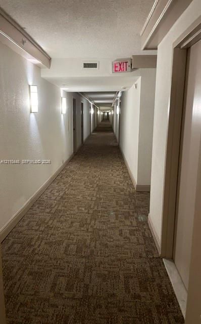 Hallway featuring wall-mounted light fixtures and patterned carpeting