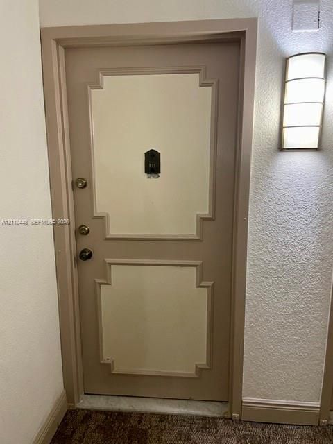 Solid core door with decorative recessed panel detailing, integrated metal peephole, brass-finished hardware, and wall-mounted arched glass sconce