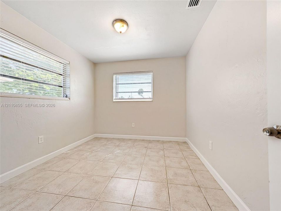 Neutral-toned room featuring ceramic tile flooring, dual windows with horizontal blinds, and a flush-mount ceiling fixture