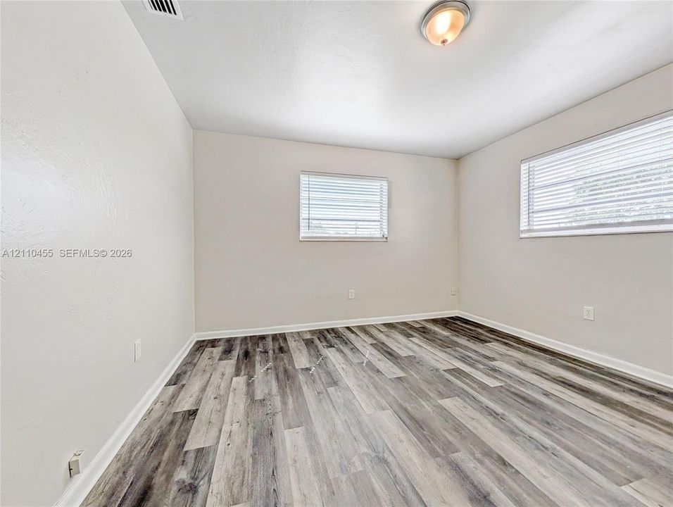 Neutral interior featuring wood-finish flooring, white walls, and multiple windows with horizontal blinds