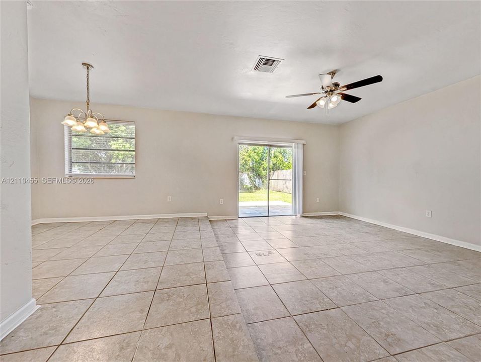 Neutral-toned ceramic tile flooring, multi-arm chandelier, ceiling fan with light kit, and glass sliding door access to exterior grounds