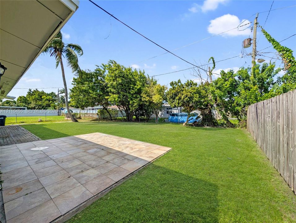 Backyard featuring a tiled patio, expansive lawn, mature landscaping, and wood privacy fencing