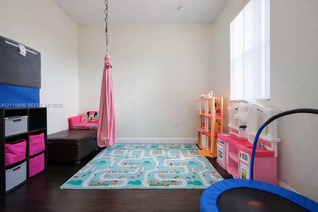 Room featuring dark wood-finish flooring, neutral walls, and a large window with vertical blinds