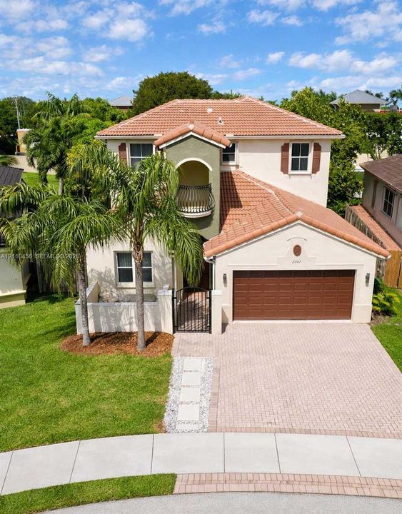 Two-story residence featuring a Mediterranean-style tile roof, decorative wrought iron balcony, paved driveway, and private courtyard entry