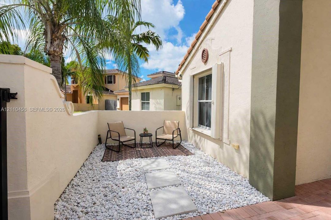 Enclosed courtyard featuring stucco walls, white decorative stone ground cover, concrete paver pathway, and tile roof detailing