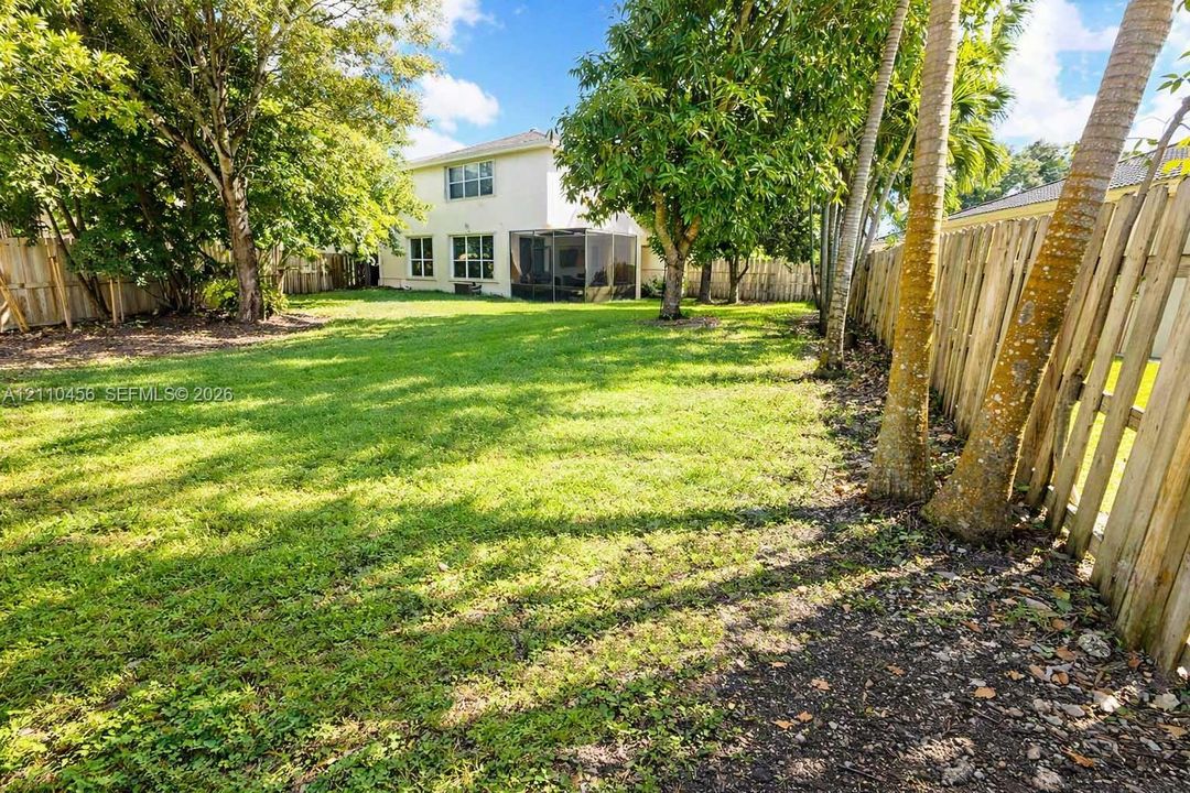 Expansive backyard featuring a large grass lawn, mature trees, wood privacy fencing, and a screened-in rear patio