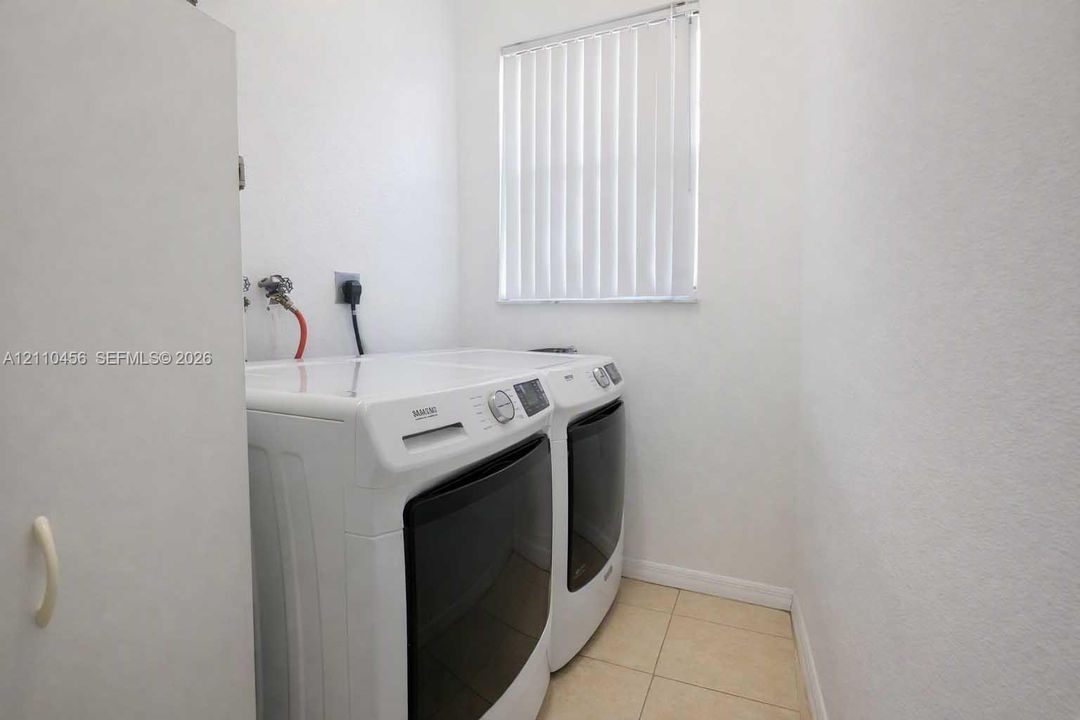 Laundry area featuring neutral tile flooring, vertical window blinds, and dedicated water and electrical hookups