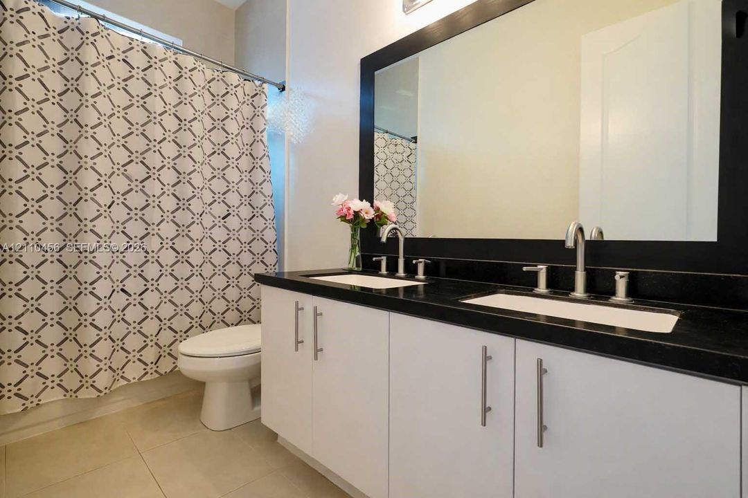 Dual-sink vanity with white cabinetry, dark stone-finish countertop, undermount basins, and a large framed mirror