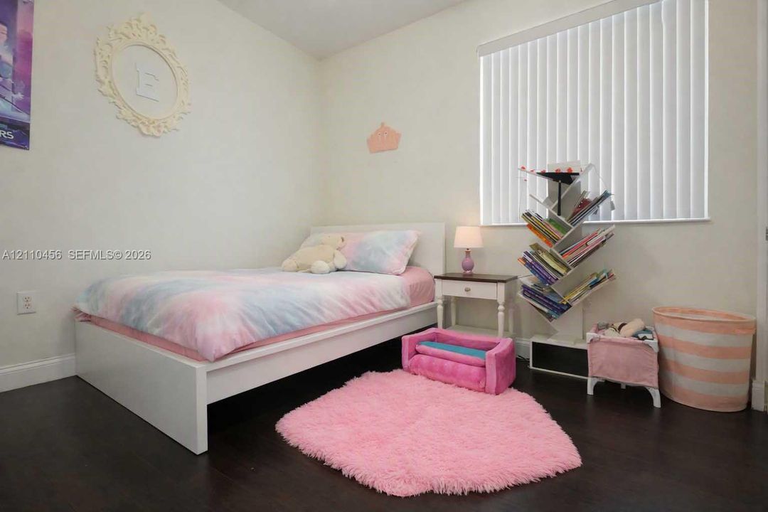 Bedroom featuring dark wood-finish flooring and vertical slat window blinds