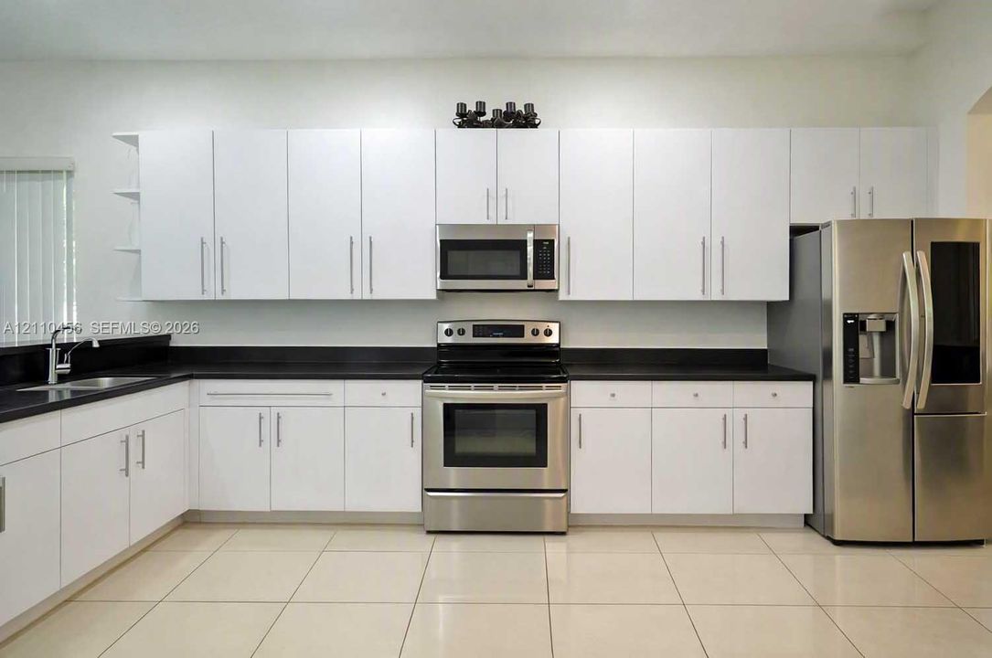 Kitchen featuring white cabinetry with brushed metal hardware, solid-surface dark countertops, stainless steel appliances, and large-format tile flooring