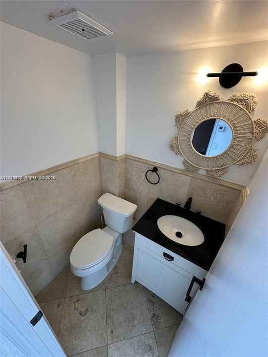 Bathroom featuring a white vanity cabinet, a dark stone-finish countertop with an integrated basin, natural stone wall tiling with decorative trim, and stone floor tiles